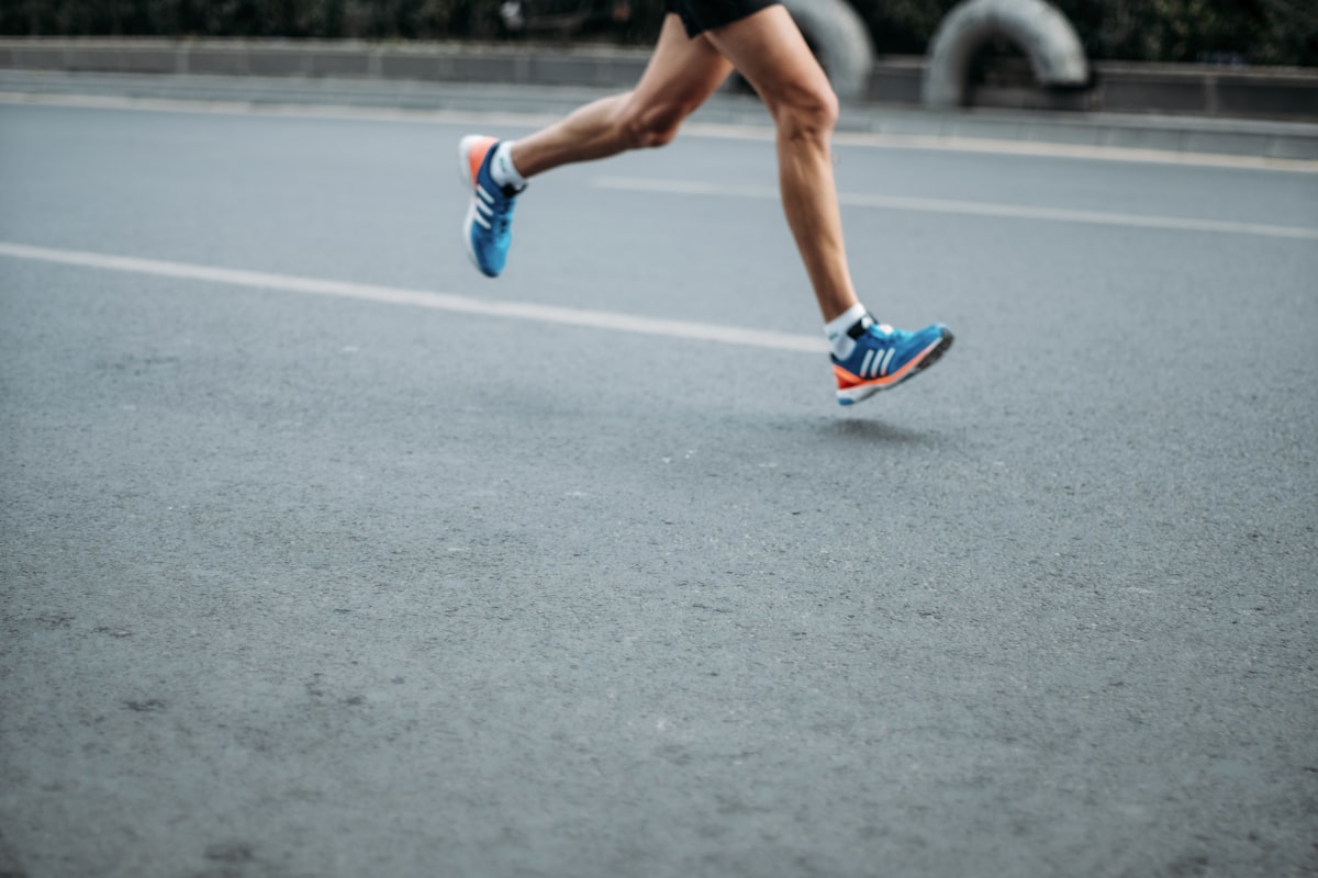 Runner mid-stride on an open road, legs and running shoes in motion
